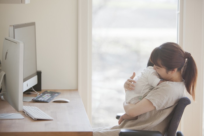 子どもを抱えてパソコンの前に座る女性